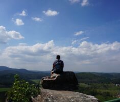 Wanderer sitzt auf Felsen und schaut über den Hunsrück